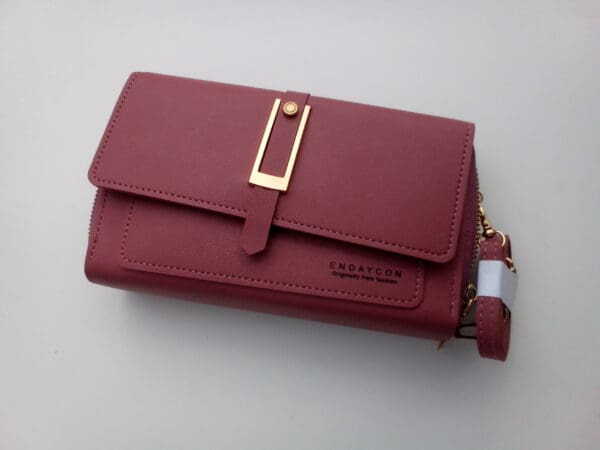 A red wallet with a gold clasp and wrist strap.