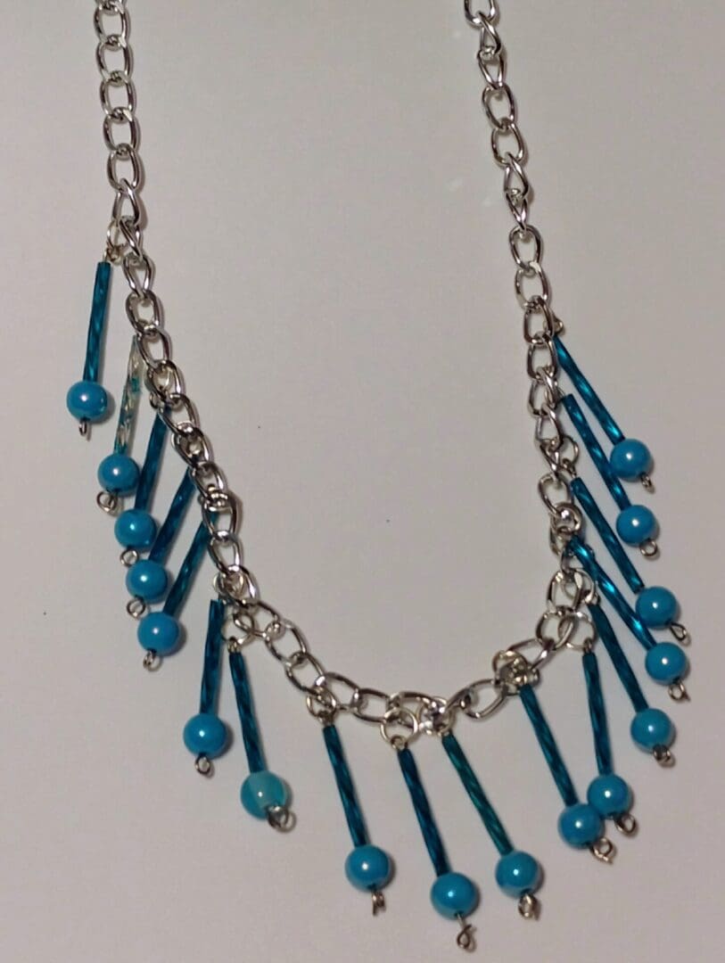Silver chain necklace with dangling blue beads and rods.